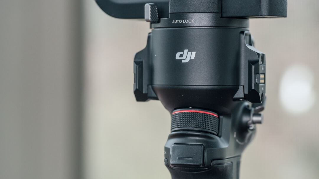 Передняя часть корпуса DJI RS 4 Pro: рифлёное колесо тонкой настройки с красной окантовкой, нажимаемая кнопка-курок под ним, маркировка AUTO LOCK и боковой порт NATO/RSA с контактной группой