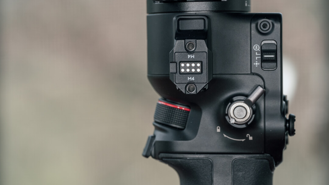 Правая боковая грань DJI RS 4 Pro: интерфейсный порт NATO/RSA с резьбой M4 и контактами питания, механический тумблер выбора режимов подвеса и переднее управляющее колесо с красным кольцом